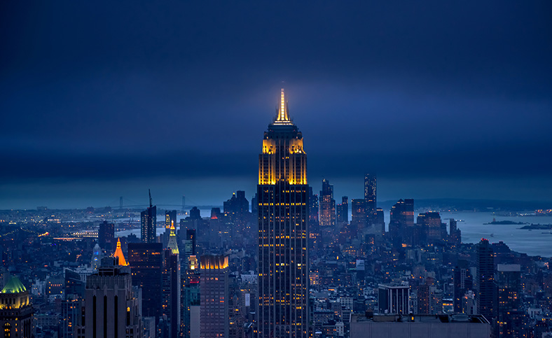 A picture of the Empire State Building in NYC at night with river in background